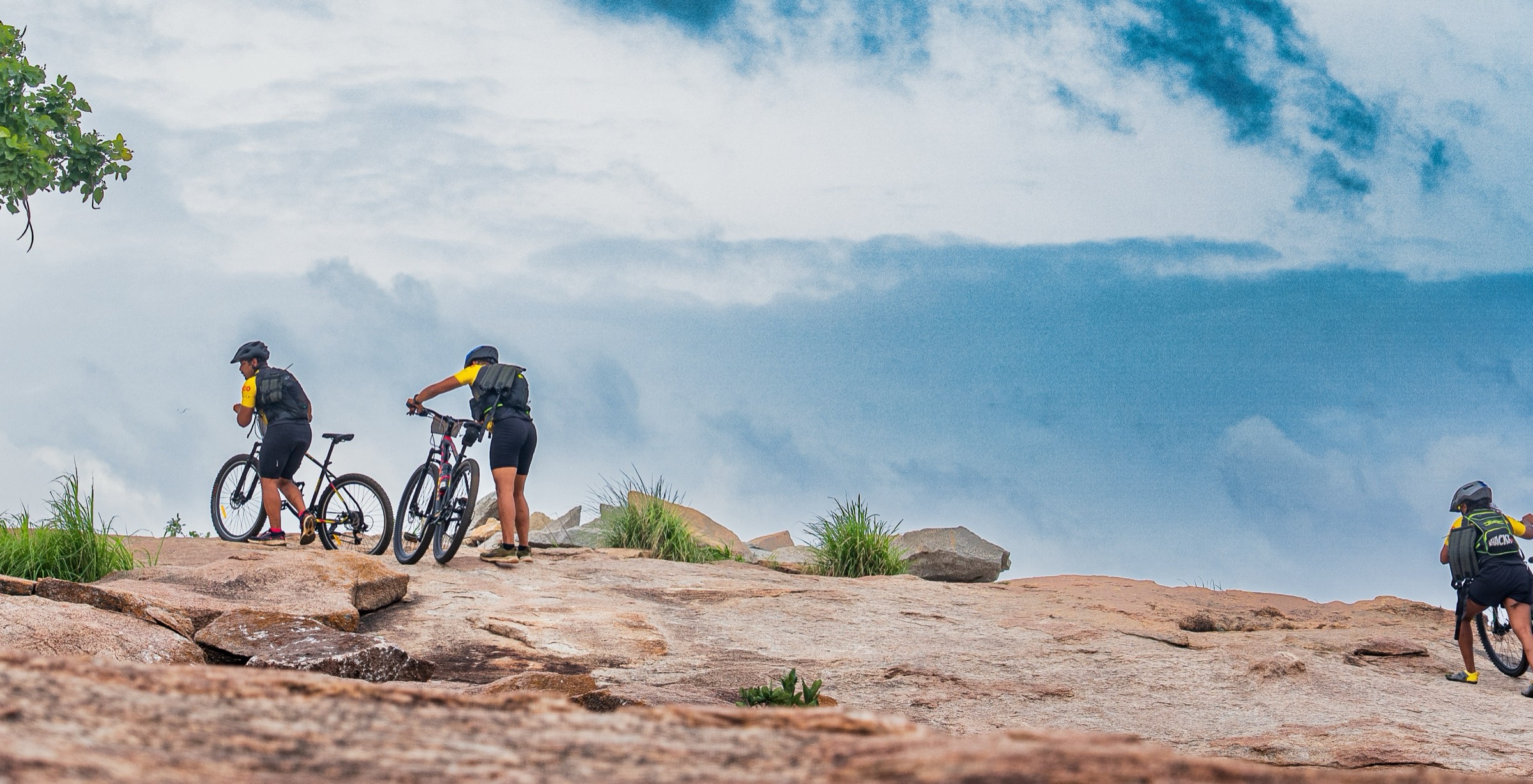 Mountain bikers pushing their bikes across a granite summit under a stormy sky