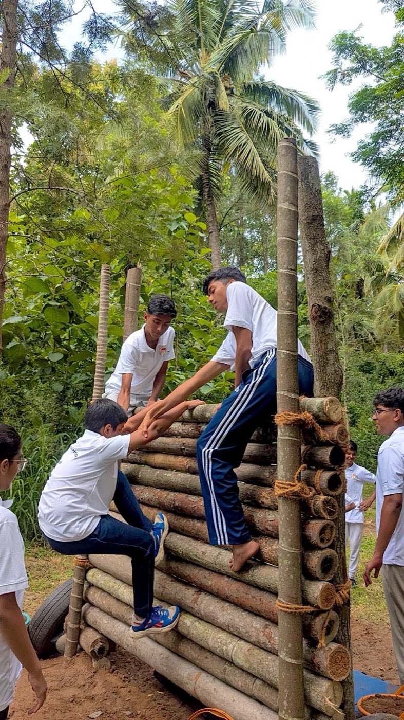 Students helping each other over a log wall at an outdoor camp